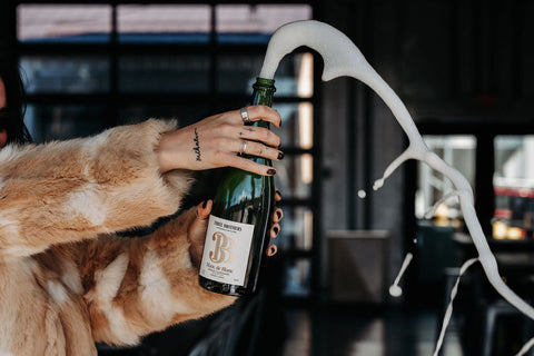 Female hands popping the cork off a bottle of Three Brothers Wineries Blanc de Blanc sparkling wine