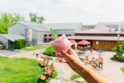 Hand holding a glass of pink frozen wine slushie overlooking Three Brothers Wineries courtyard