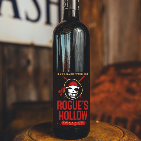 Bottle of Rogue's Hollow red wine on a wooden barrel with a rustic background.